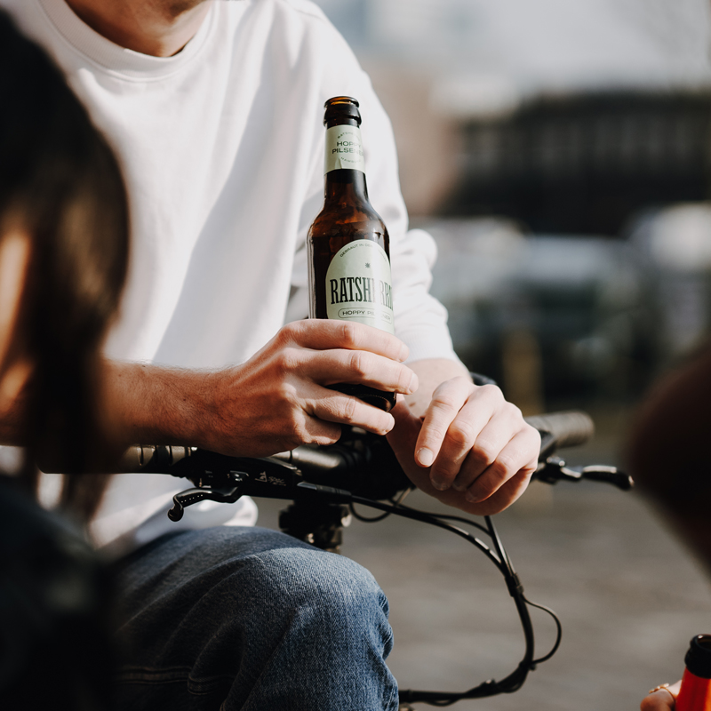 Bierflasche von Mann gehalten, der sich auf einem Fahrradlenker abstützt.