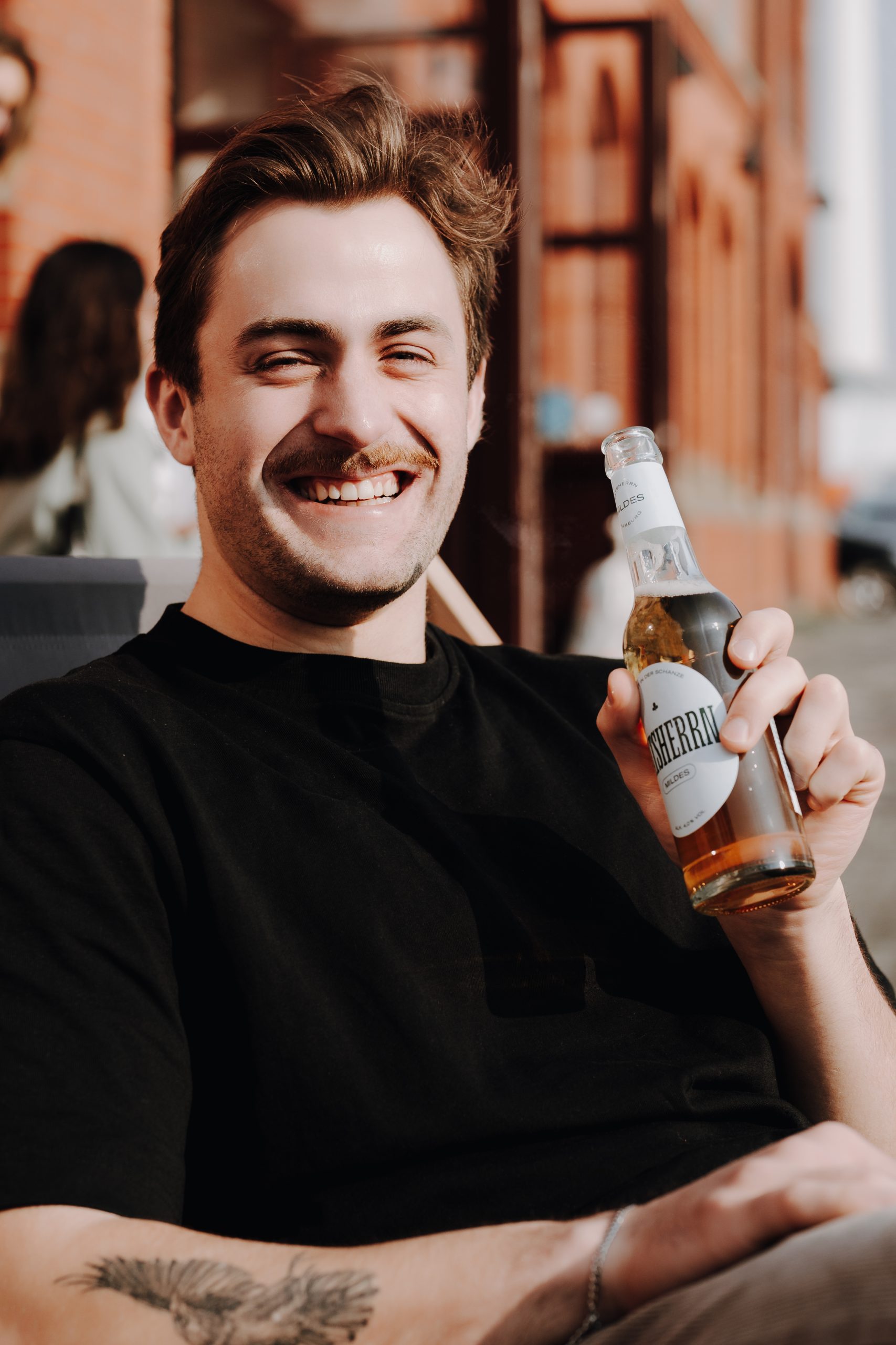 Junger Mann sitzt lachend vor Ratsherrn Store mit Ratsherrn Bier in der Hand